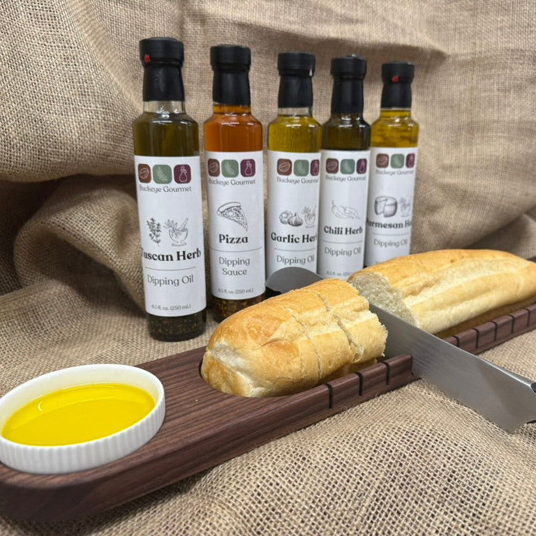 Set of olive oil bottles with dipping oils and bread on a wooden board against a textured fabric background.