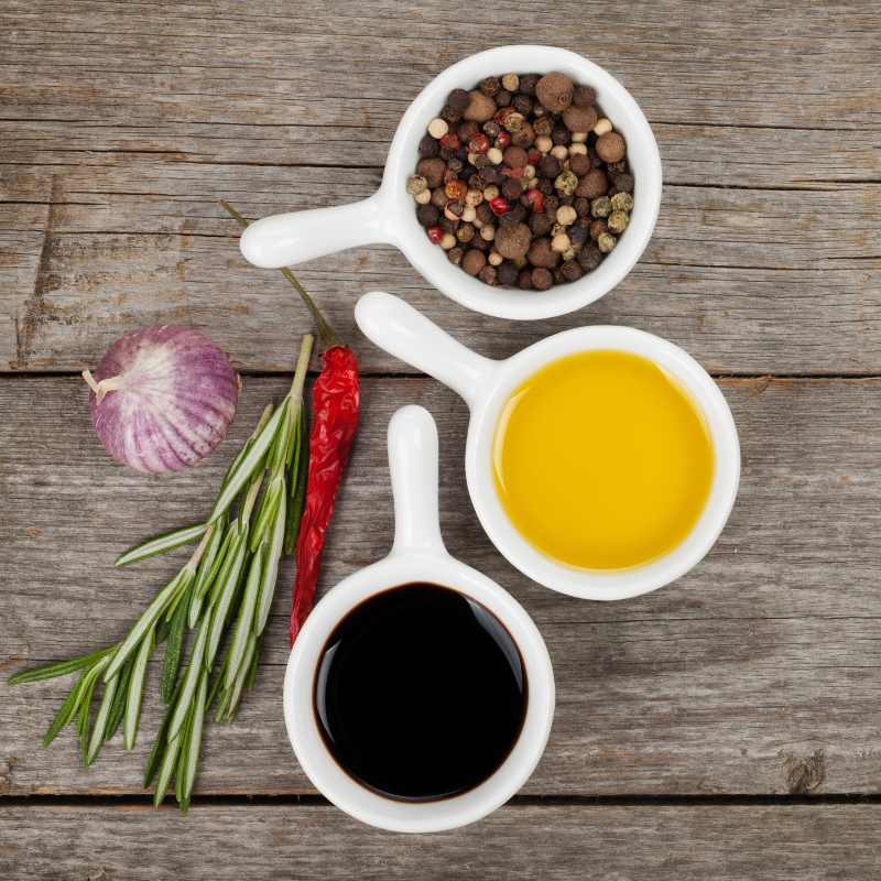 Assorted Buckeye Blends condiments in white ceramic spoons on rustic wooden table: garlic, rosemary, chili, olive oil, and balsamic vinegar.