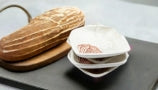 Three small seashell shaped dishes on top of a black cutting board with a small loaf of bread next to them. 