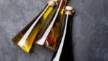 Three triangular glass bottles with yellow, red, and black liquid inside on a gray table top. 