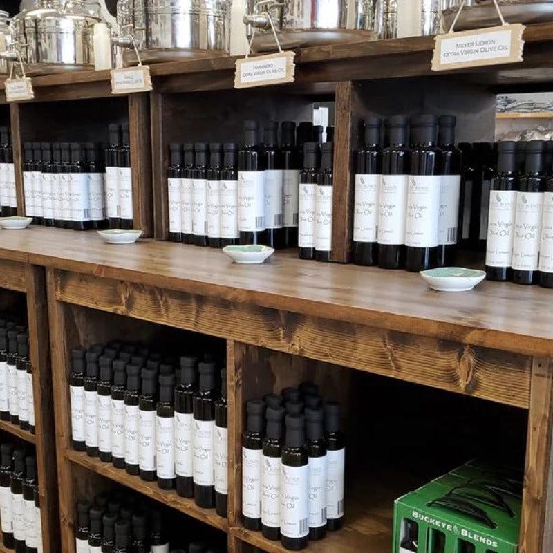 Wooden shelves stocked with a variety of Buckeye Blends balsamic vinegars and olive oils in a store.