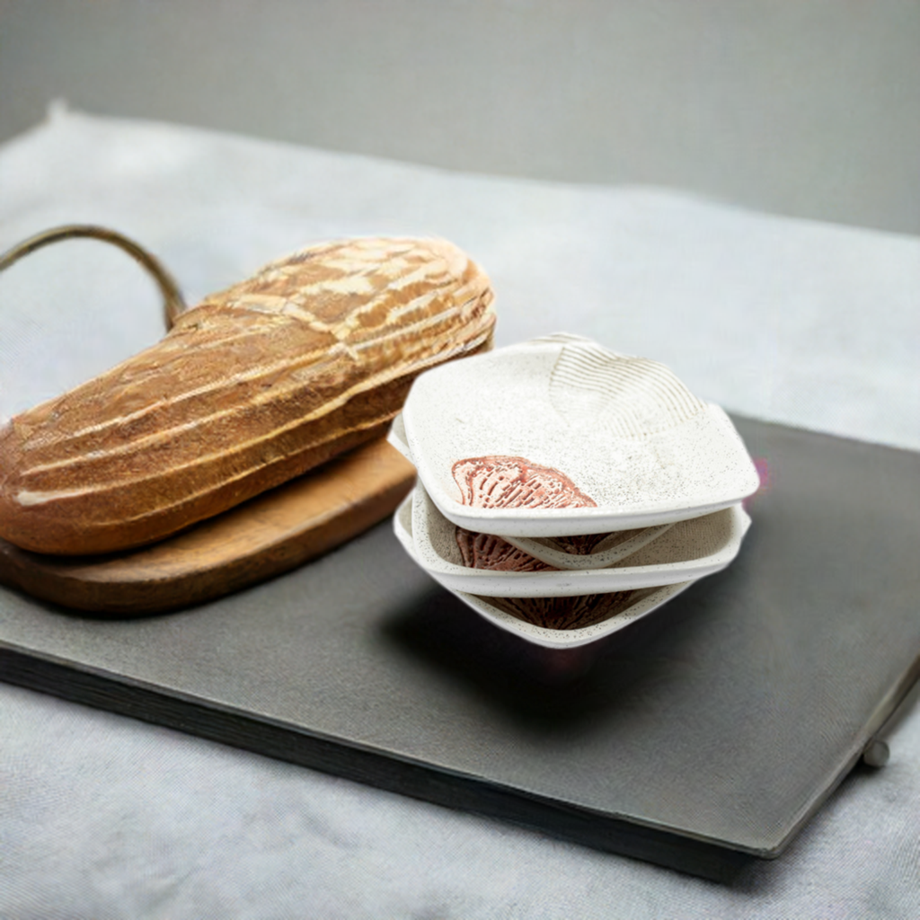 A white ceramic dipping plate with a garlic print design sits on a black serving platter. Next to it, a fresh loaf of bread rests on a wooden cutting board.